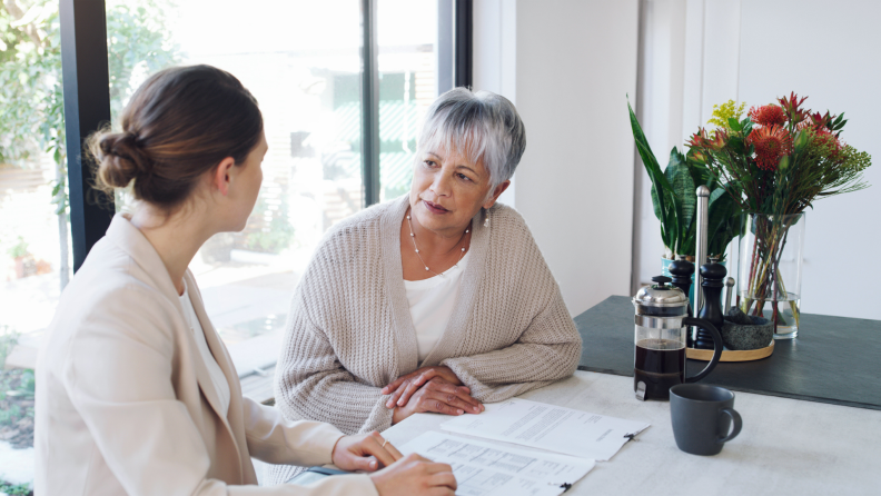 Older person sitting down with specialist in front of paperwork.