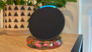 The Amazon Echo Pop sits on a wooden table in front of a plant.