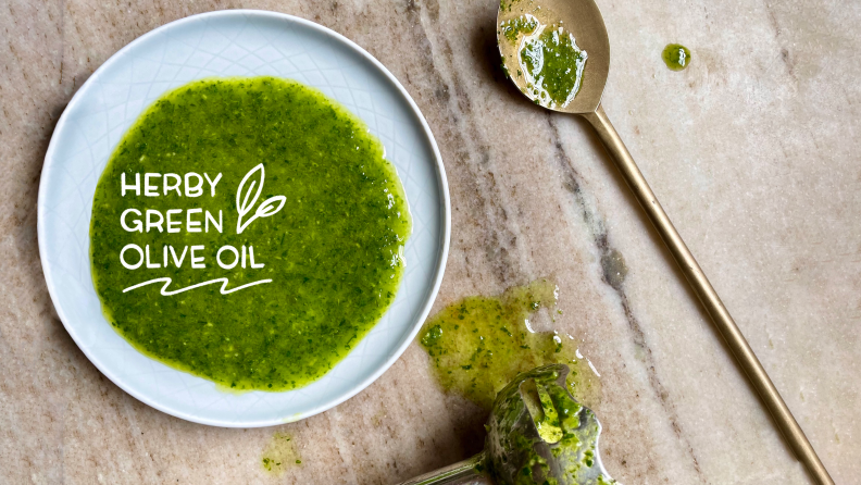 A bowl of herby green olive oil next to a spoon