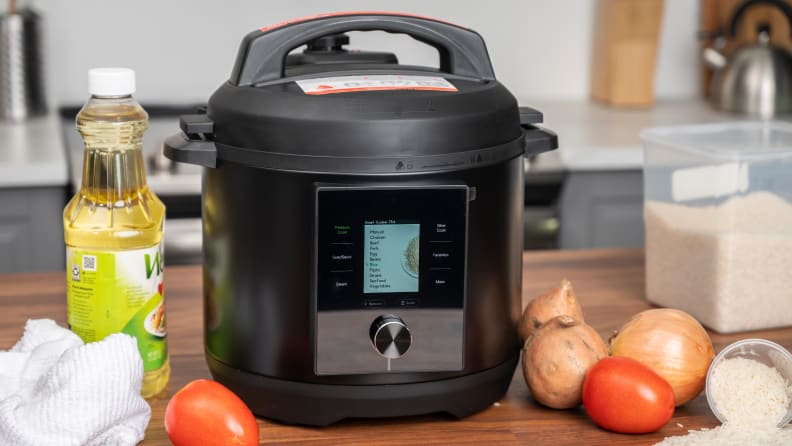 The Chef iQ pressure cooker sits on a white tiled counter accompanied by fresh produce on a cutting board.
