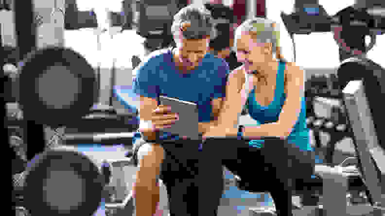 Two people sitting on a workout bench at the gym.