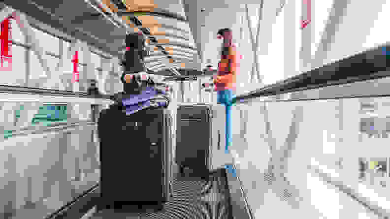 Two women stand on an airport people mover, holding on to their luggage