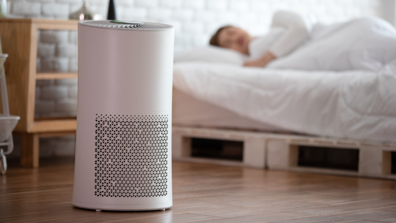 An air purifier sits in a room while a person sleeps.