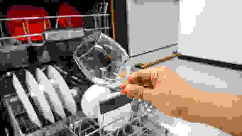 A person holding a clear wine glass outside the Bosch 800 Series dishwasher.