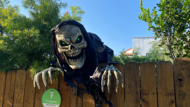 A 6-foot-tall Grim Reaper looking over a fence with glowing green eyes