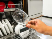 A hand holding up a dry, spotless glass in front of a Bosch dishwasher