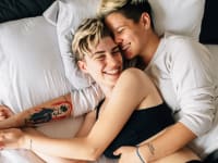 A queer couple cuddles in bed together, one spooning the other.