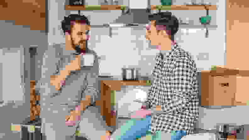 Gay partners sit on the kitchen counter drinking coffee