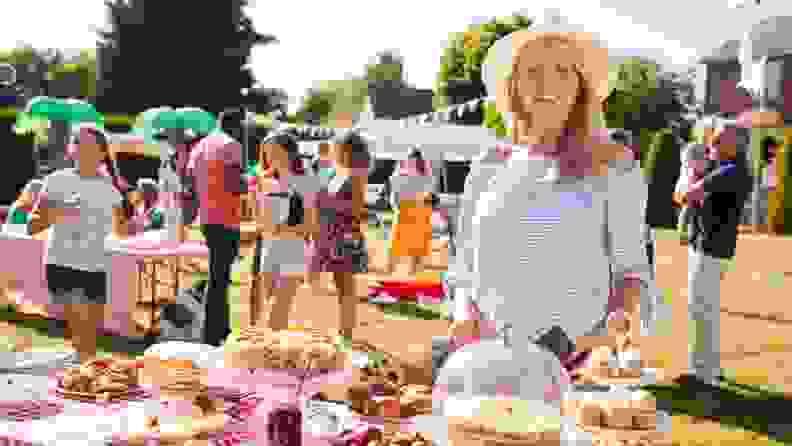 Portrait of mature woman serving on cake stall at busy summer garden fete.