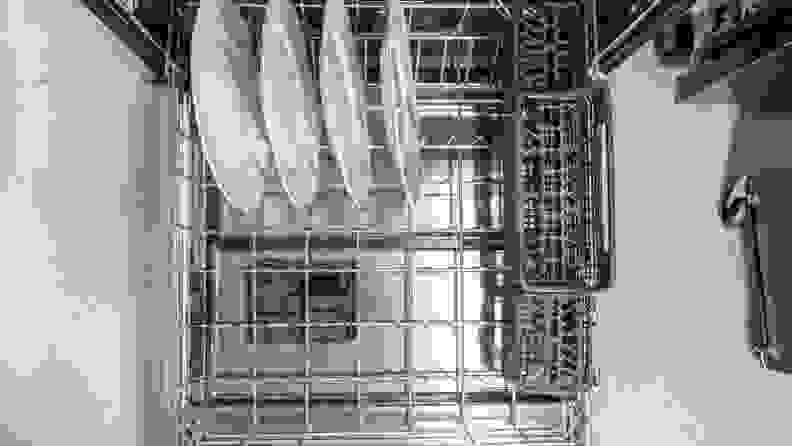 The lower rack of a dishwasher is filled with four white plates