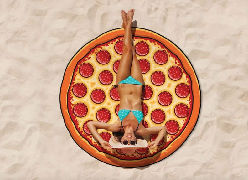 Woman sitting on large pizza shaped towel on the beach.
