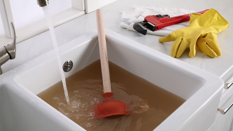 A sink plunger sits in a clogged kitchen sink.