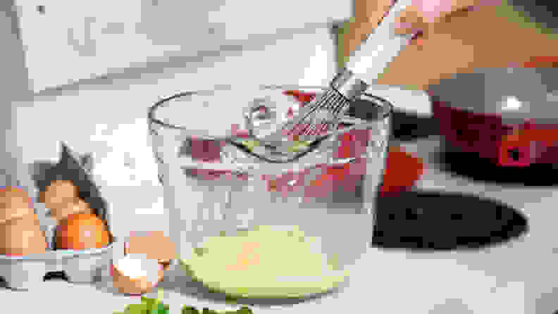 A person whisks together the ingredients for an omelette in a glass bowl.