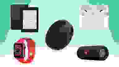 Black Kindle tablet, red Apple smartwatch, black Eufy robot vacuum, black JBL bluetooth speaker, and Apple Airpods in front of green background.