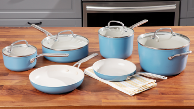 Blue and white pans and pieces from the KitchenAid cookware set sitting atop a wooden table.