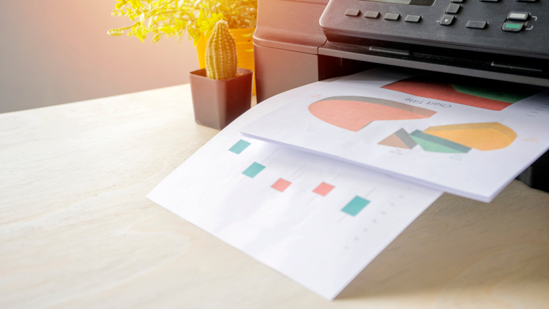 Stock image of several sheets of paper sticking out of a printer with various charts on them.