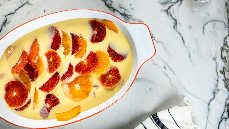 A orange and citrus fruit tart is in an oval-shaped baking dish on a marble tabletop.