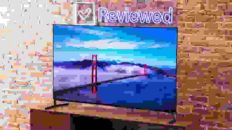 The Sony A95L QD-OLED TV positioned in front of a brick wall displaying a high-resolution image of the Golden Gate Bridge amidst heavy cloud cover