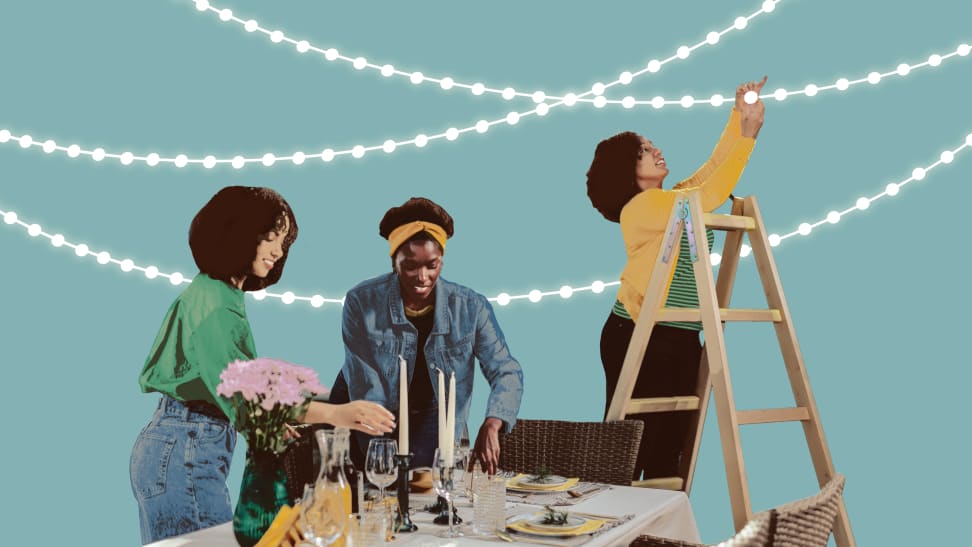 A group of people setting up a patio table and some hanging lights.