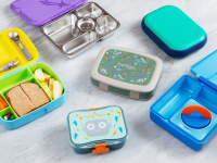 A variety of brightly colored lunch boxes sit open and closed on a marble counter.