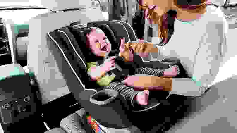 A smiling baby getting put into a carseat