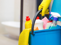 A person holds the handle of a bucket filled with bathroom cleaning supplies.