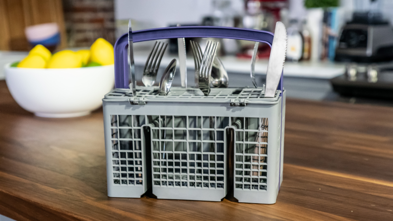 A dishwasher's cutlery basket sits on a counter in front of a bowl of lemons