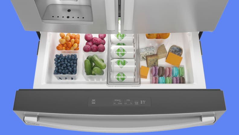 The bottom drawer of an open fridge showcases fresh fruit, drinks, and sweets.
