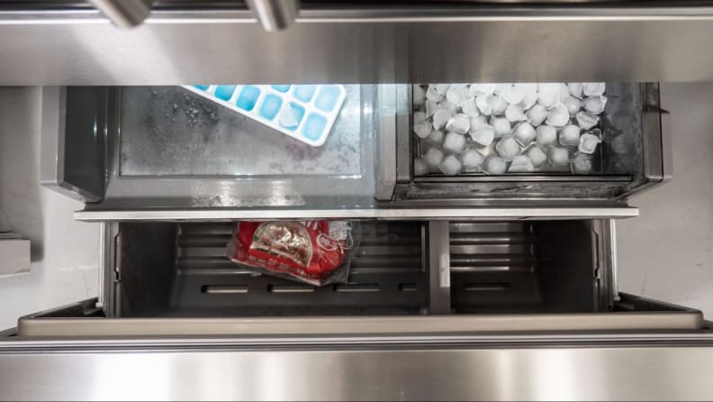 Freezer with the extra ice-maker. Trays of ice cubes and some bread lies inside.