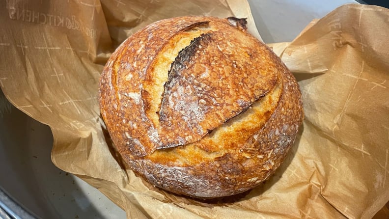 A freshly baked round loaf of sourdough bread siting in parchment paper inside a Dutch oven.