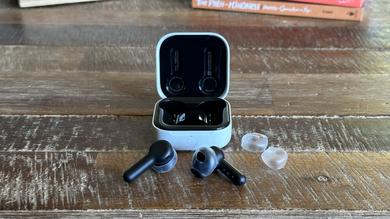 The Amazon Echo Buds and included ear tips sitting in front of their open charging case on a wooden table.