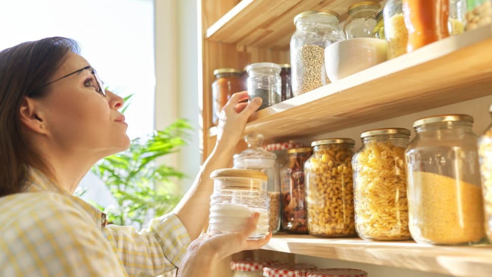 A woman holds a jar of sugar inside her organized pantry full of canned items.