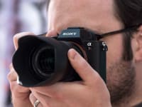 A photographer holds a camera viewfinder up to their eye to compose a shot.