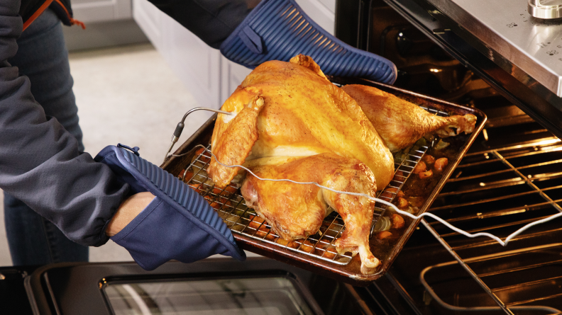A person removing a roasted spatchcocked turkey from the oven