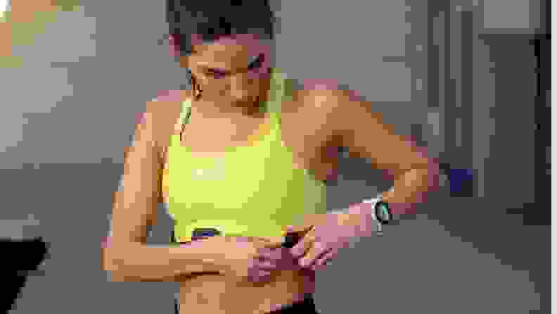 A woman in a yellow tank top adjusts her Garmin HRM-Fit monitor.
