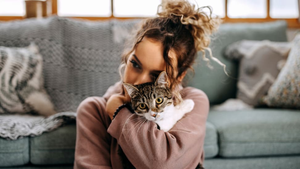 Young woman hugging her cat in front of couch