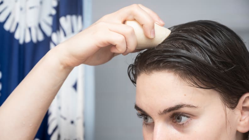 A closeup of a person holding the HiBar Volumize Shampoo Bar up to their wet hair in the shower.