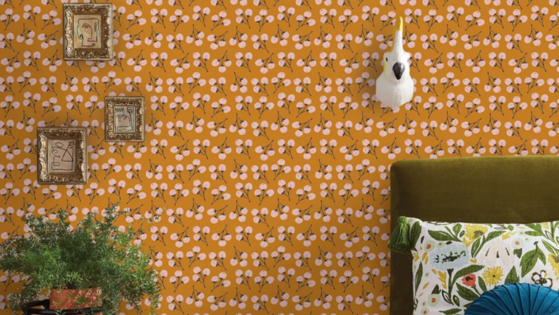 An orange wallpaper with lollipop style florals. Three small picture frames hang on the wall on the left side of the photo. On the right a parrot bust hangs on the wall over a bed.