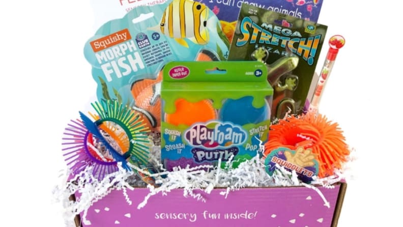 A box bursting with sensory toys, including play foam, megastretch, and squigglets