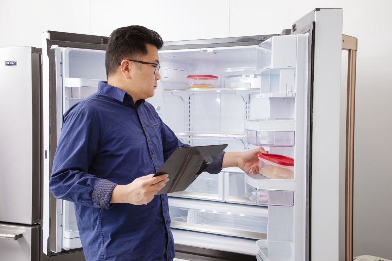 An Asian man places a plastic container of goo into an open refrigerator