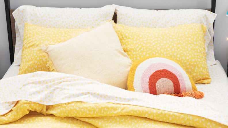 Pillows and throw pillows sit on a yellow comforter in a dorm room.