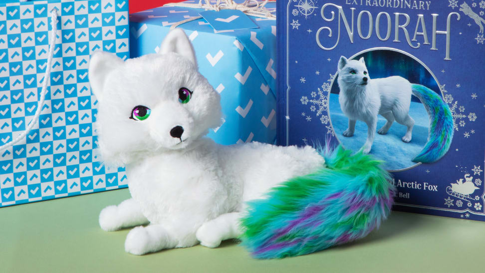 A white fox with green tail sits in front of a purple book and blue gifts