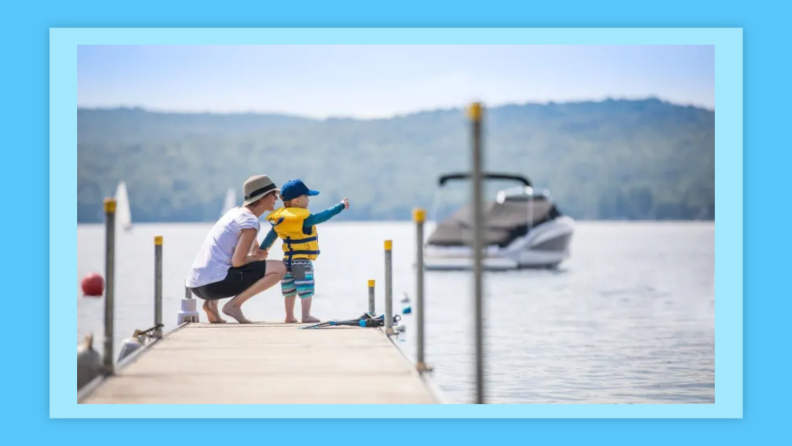 Mother and Son Looking at the View on Pier in Summer, there are boat and sailing boat in the background.