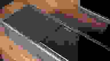 索尼的全黑音响板放在一张木桌上，左边中间的一块玻璃面板上闪烁着银色的索尼标识，旁边是覆盖着声学织物的驱动装置。