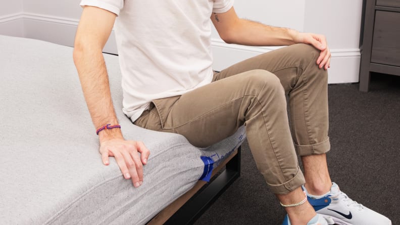 A person sitting on the edge of the mattress as the mattress itself gives out with no support.