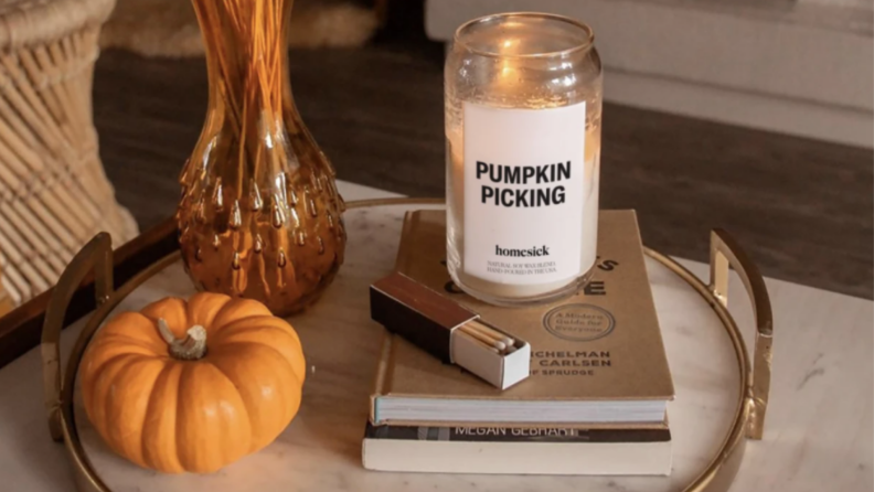 A pumpkin candle sitting on two books next to matches, a vase, and a mini pumpkin on a marble tray.