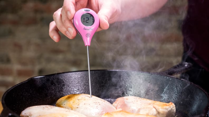 Thermopop meat thermometer taking temperature of food in a cast iron skillet outdoors.