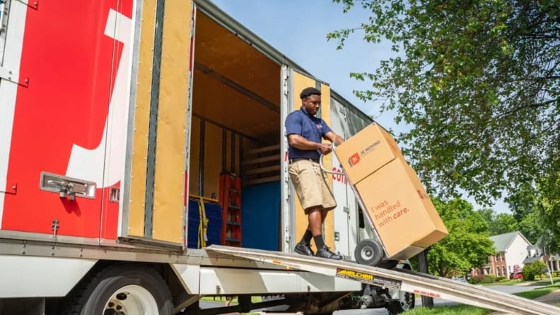 A mover unloading boxes from a truck using a ramp