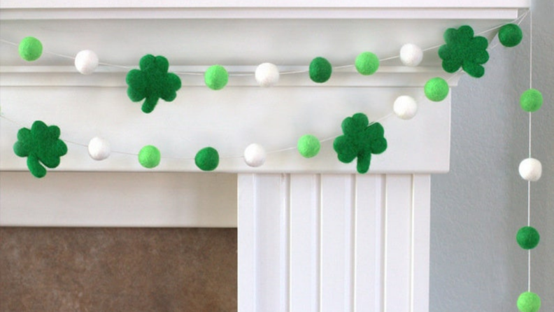 Green pom pom shamrock shaped garland hanging on mantle.