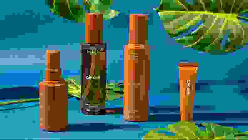 Four bottles and tubes of skincare against a blue background and foliage.
